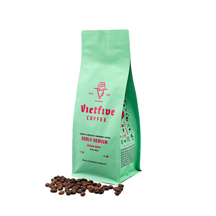 A green bag of Vietfive Coffee's Early Heaven medium roast coffee beans. The bag is standing upright with coffee beans scattered in front of it.