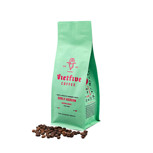 A green bag of Vietfive Coffee's Early Heaven medium roast coffee beans. The bag is standing upright with coffee beans scattered in front of it.