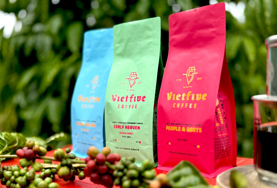 Three colorful coffee bags from Vietfive Coffee on a table with coffee beans and a cup in the background.